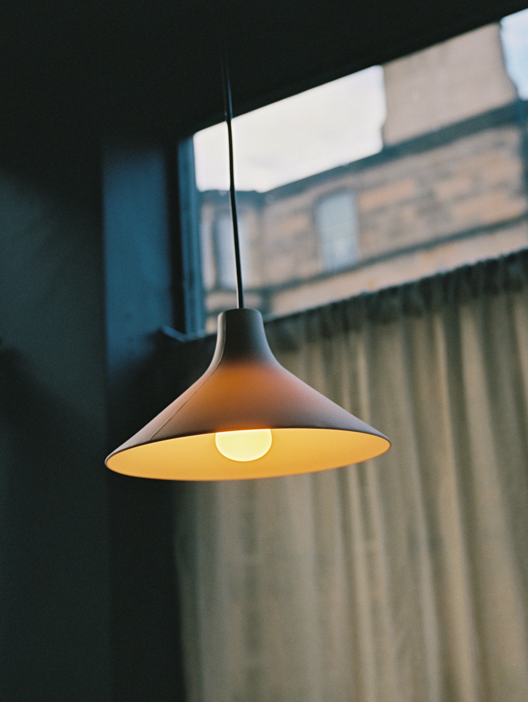 A pendant lamp lit in the window at Cardinal